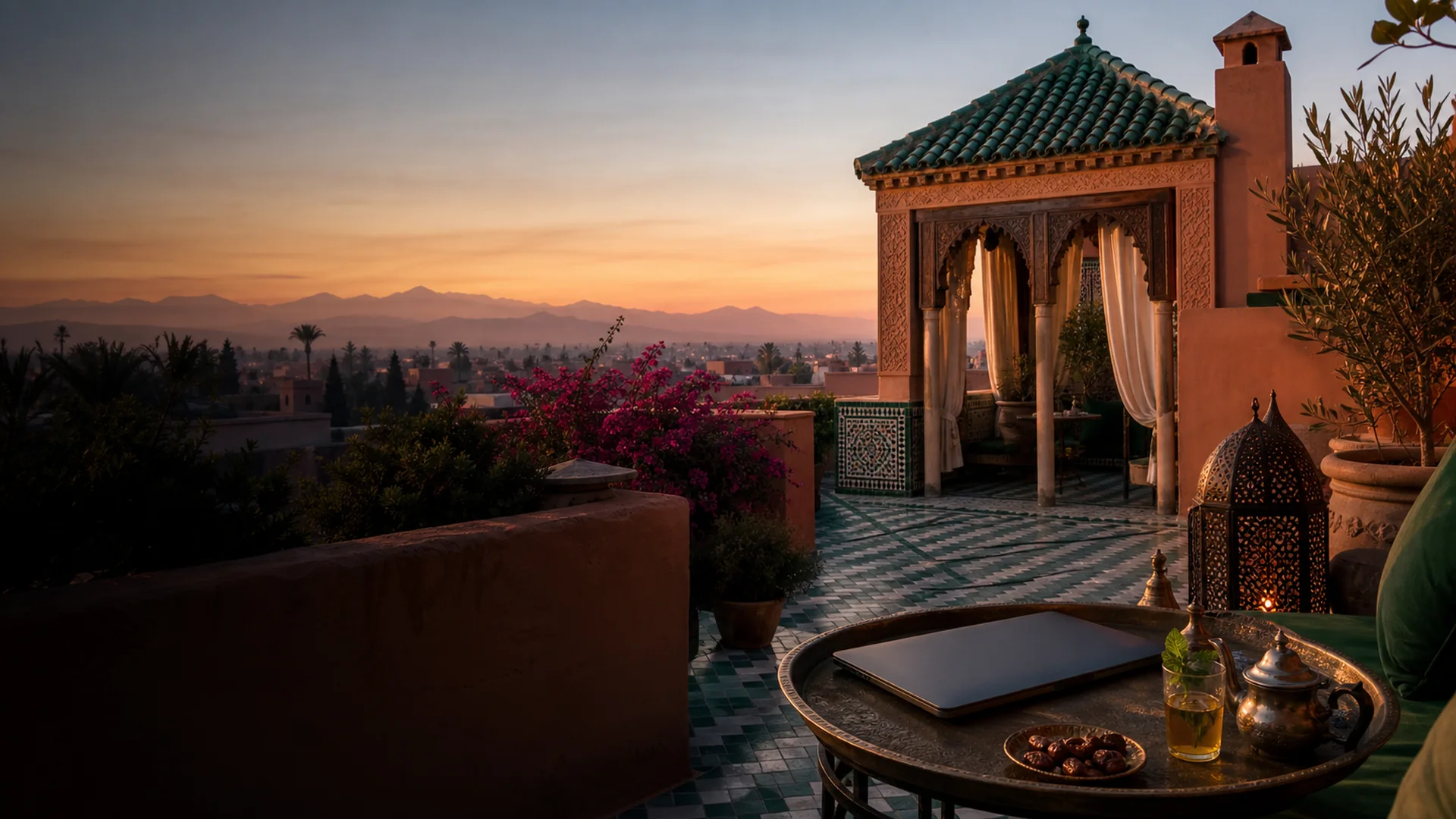 Rooftop-Terasse mit Laptop in Marrakesch – rote Lehmarchitektur und Atlasgebirge im Hintergrund